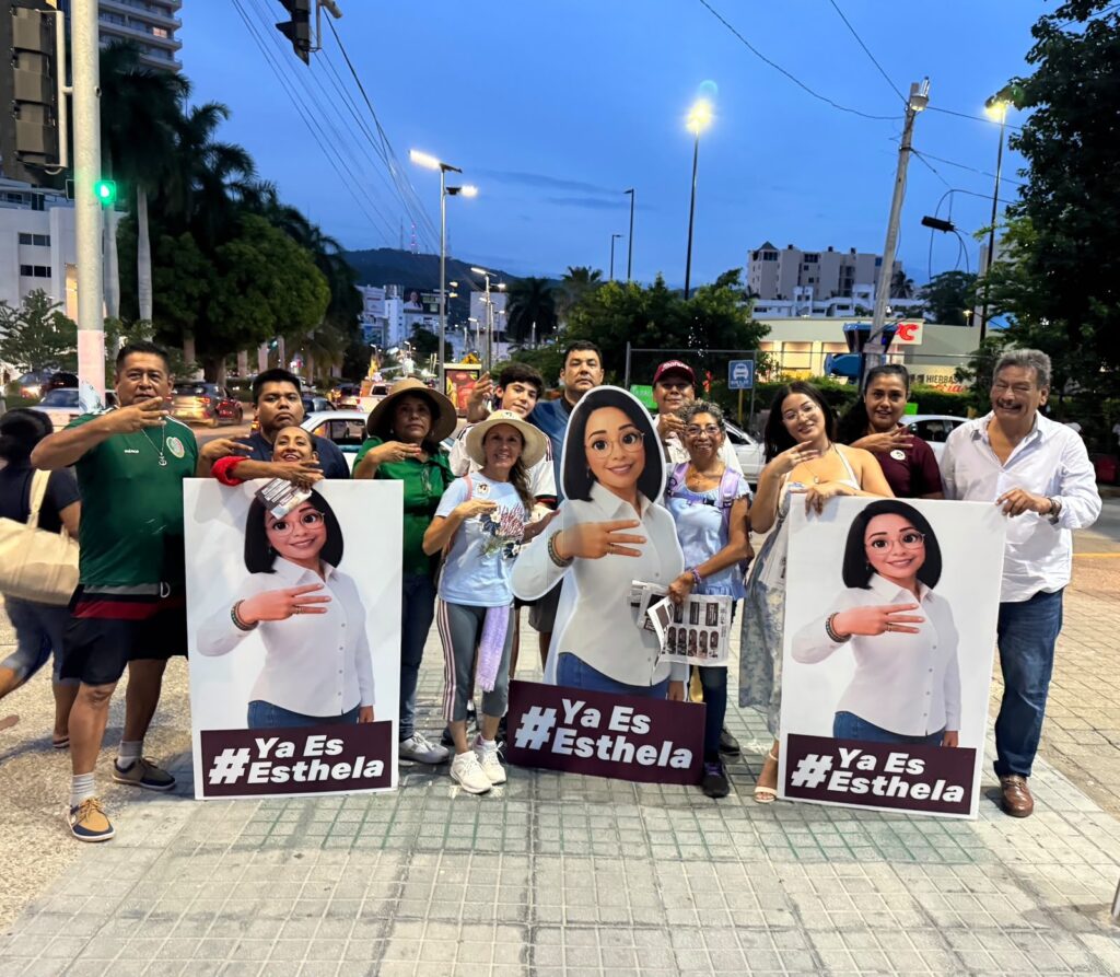 Brigadistas con figuras y el lema #YaEsEsthela en una avenida al anochecer