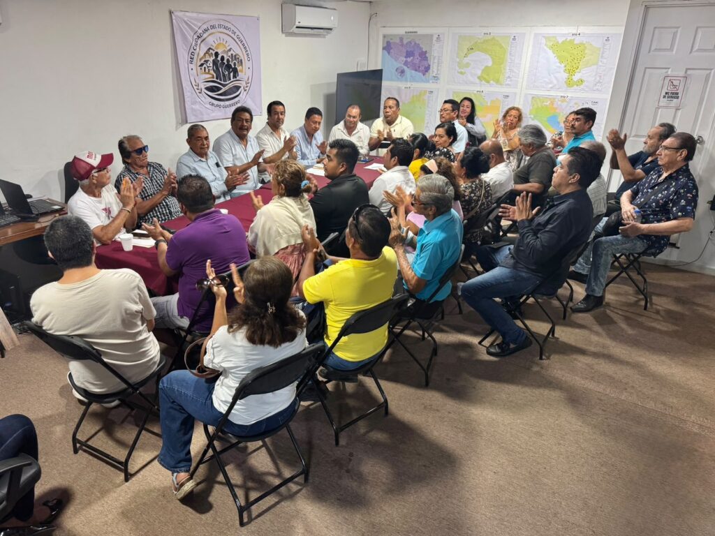 Asistentes aplauden durante una reunión, frente a mapas del estado de Guerrero