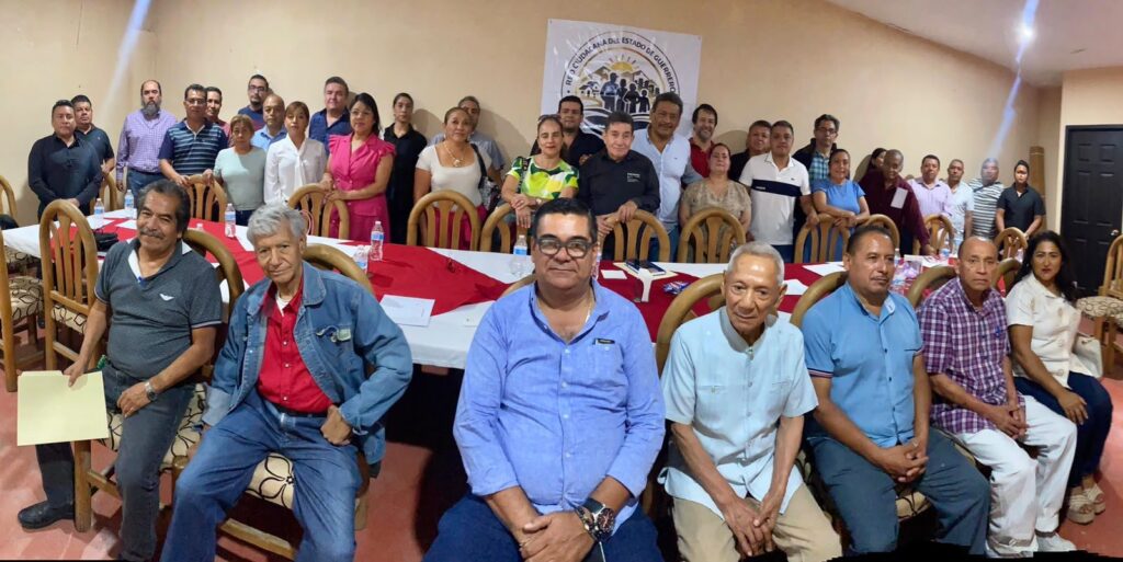 Asistentes sentados frente a una mesa con manteles rojos durante una reunión